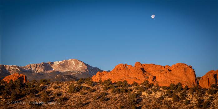 The moon sets as the morning sun lights up the Garden of the Gods and Pike's Peak in Manitou Springs, Colorado.